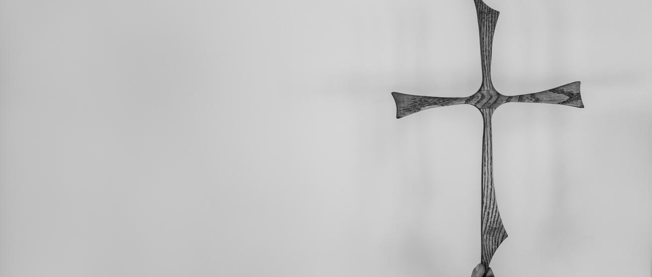Das Bild zeigt ein Kreuz, das leicht von einer Hand gehalten wird