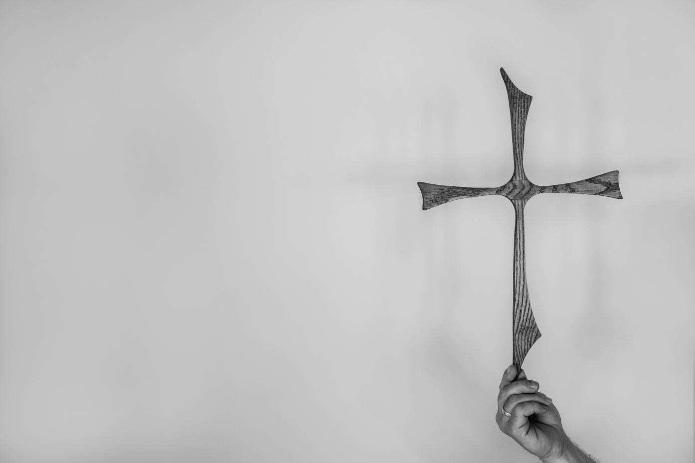 Das Bild zeigt ein Kreuz, das leicht von einer Hand gehalten wird