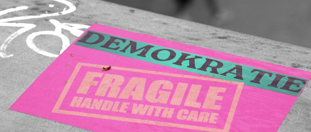 eine pinke Karte mit dem Schriftzug Demokratoe fragile handle with care