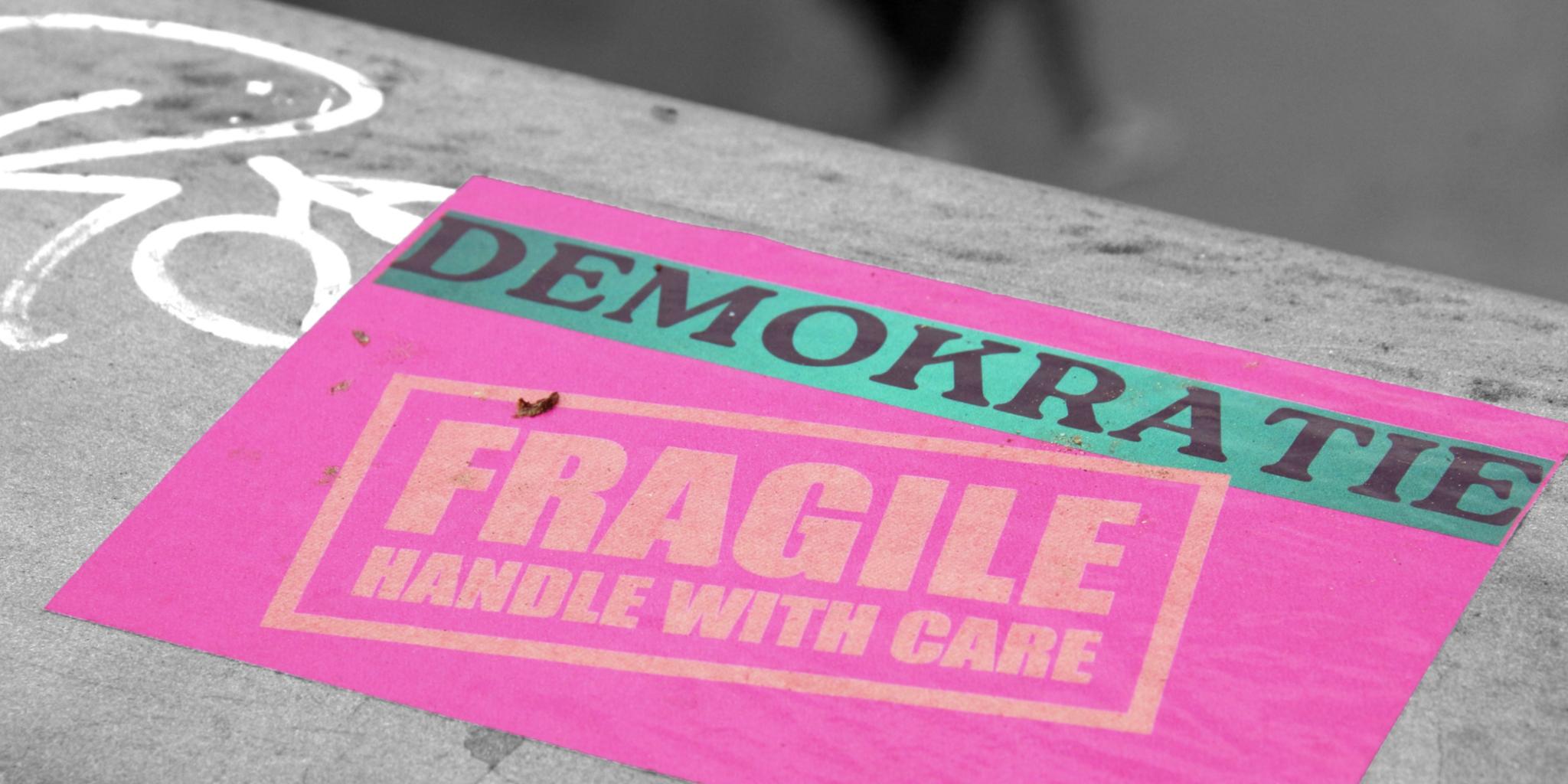 eine pinke Karte mit dem Schriftzug Demokratoe fragile handle with care