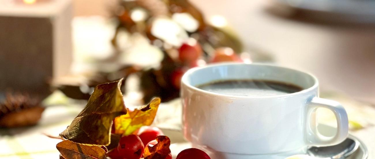 auf einem herbstlich mit Hagebutten und Äpfeln gedeckten Tischs steht eine weiße Tasse Kaffee