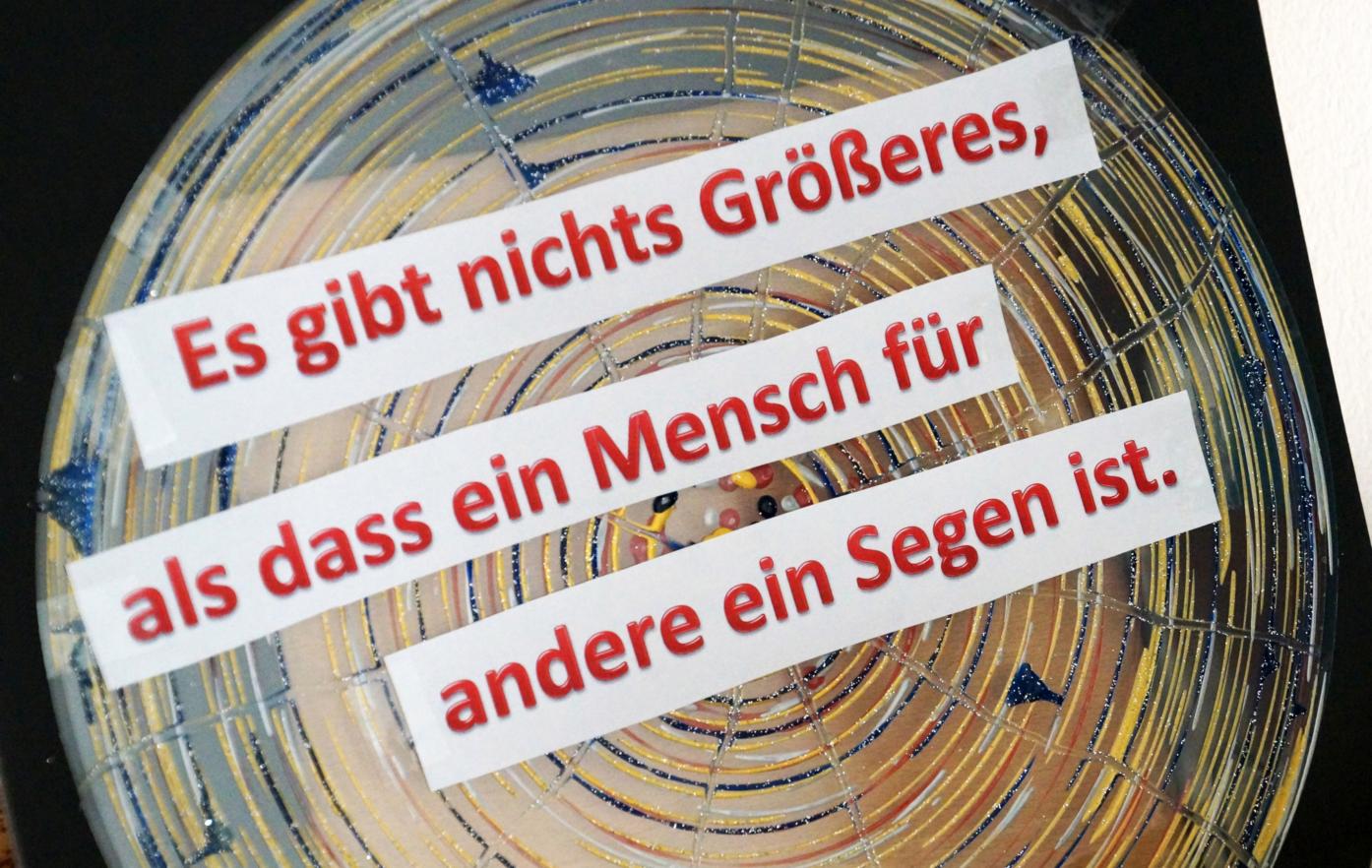 eine Holzscheibe, darüber in rot der Schriftzug: Es gibt nichts Größeres, als das ein Mensch für andere ein Segen ist.
