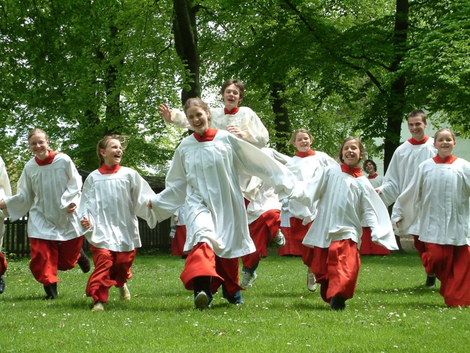 in einem Park laufen acht Messdienerinnen in rot weißen Gewändern auf uns Bildbetrachterinnen zu