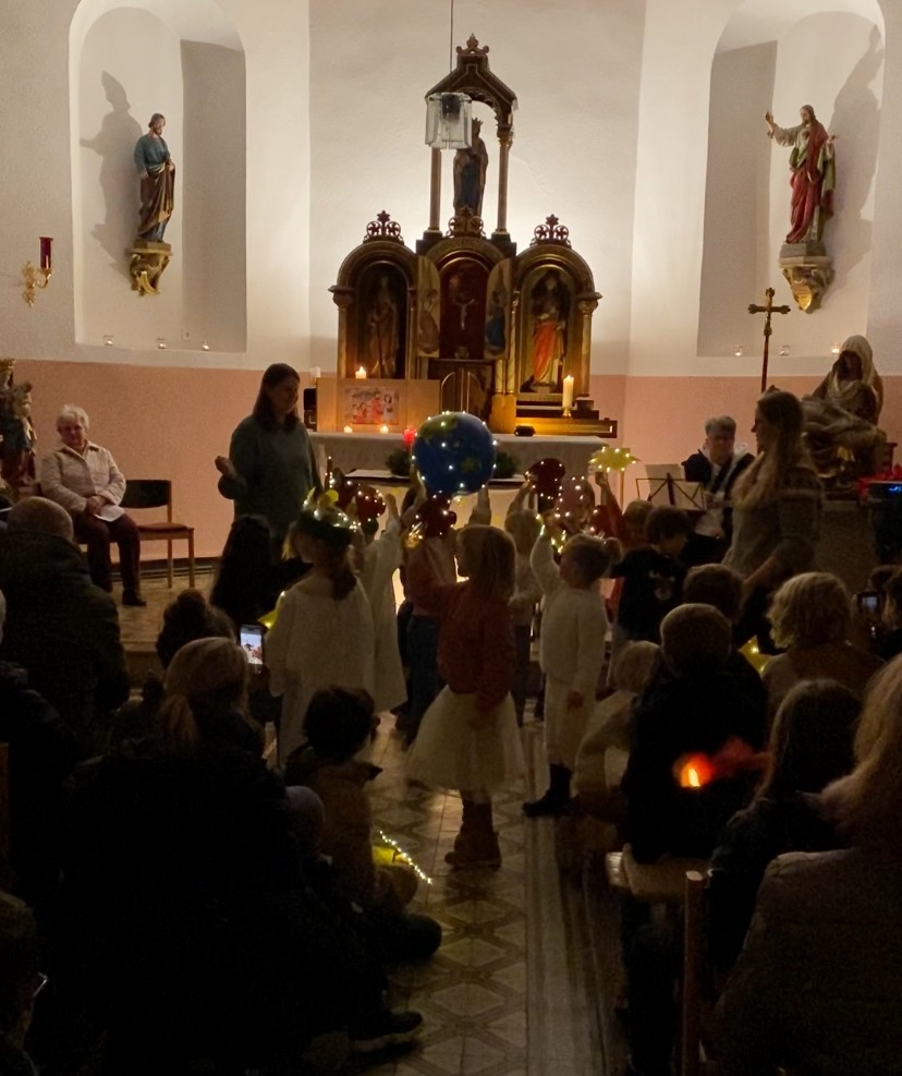 Blick in die Kapelle in Filsch, viele Menschen sitzen auf Stühlen, vor dem Altar tanzen Kinder einen Lichterztanz