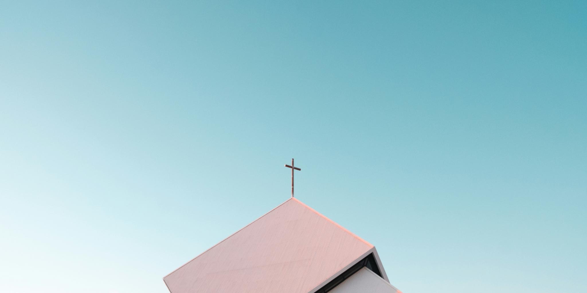 ein Kirchendach mit Kreuz vor einem blauen Himmel