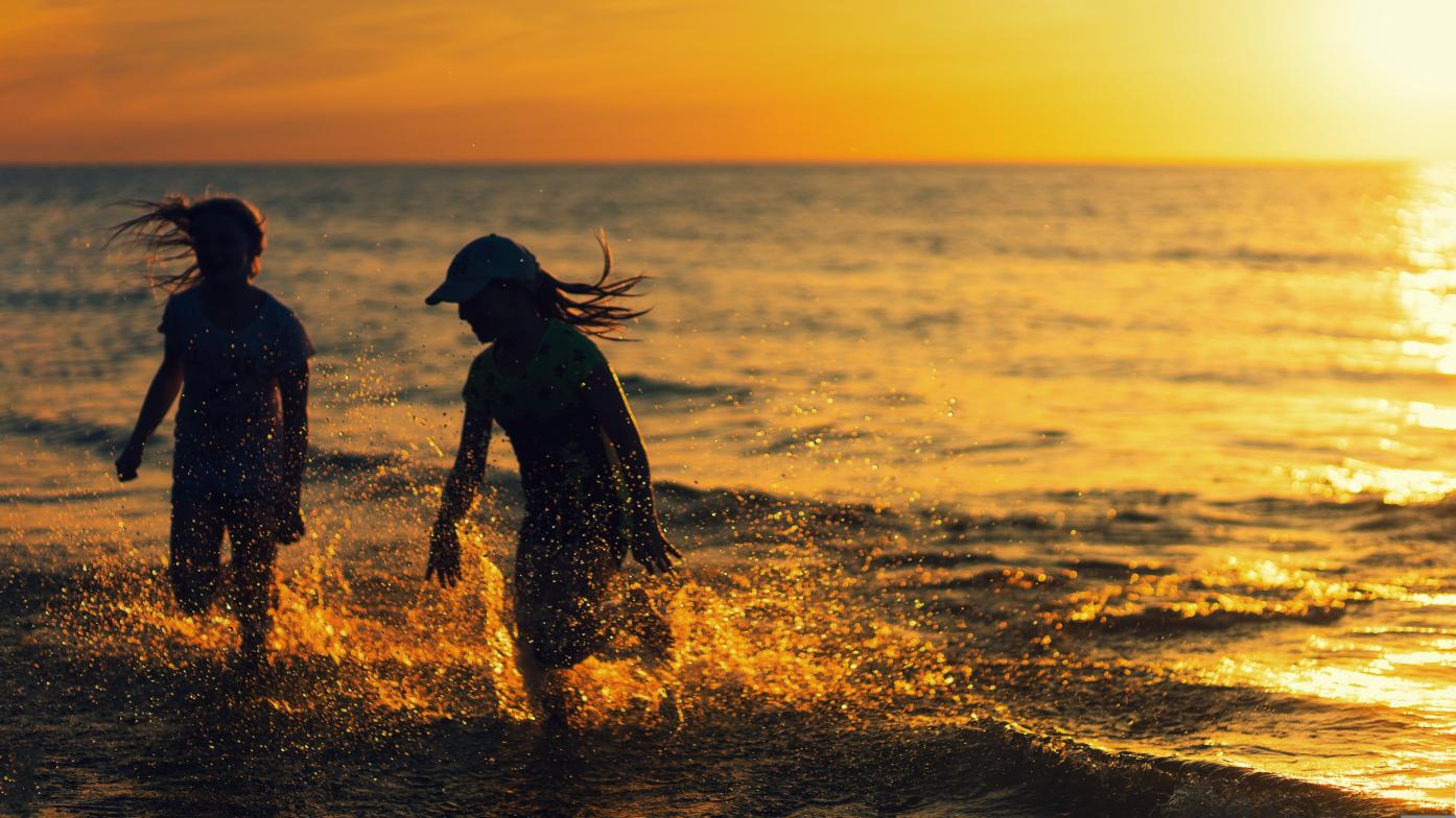 2 Mädchen laufen bei Sonnenuntergang durch das seichte Meerwasser