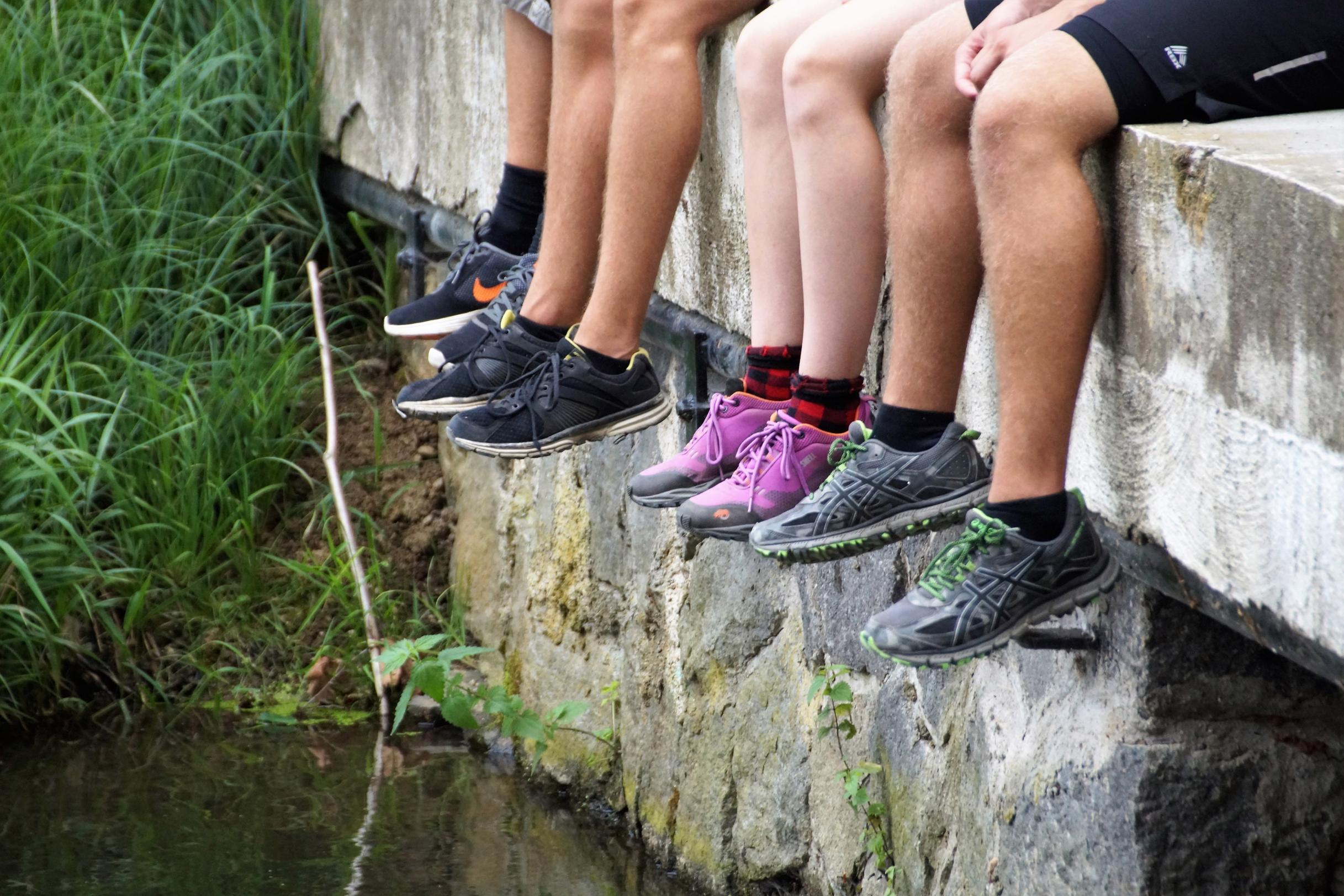 Vier Personen sitzen mit baumelnden Beinen an einer Steinmauer über Wasser