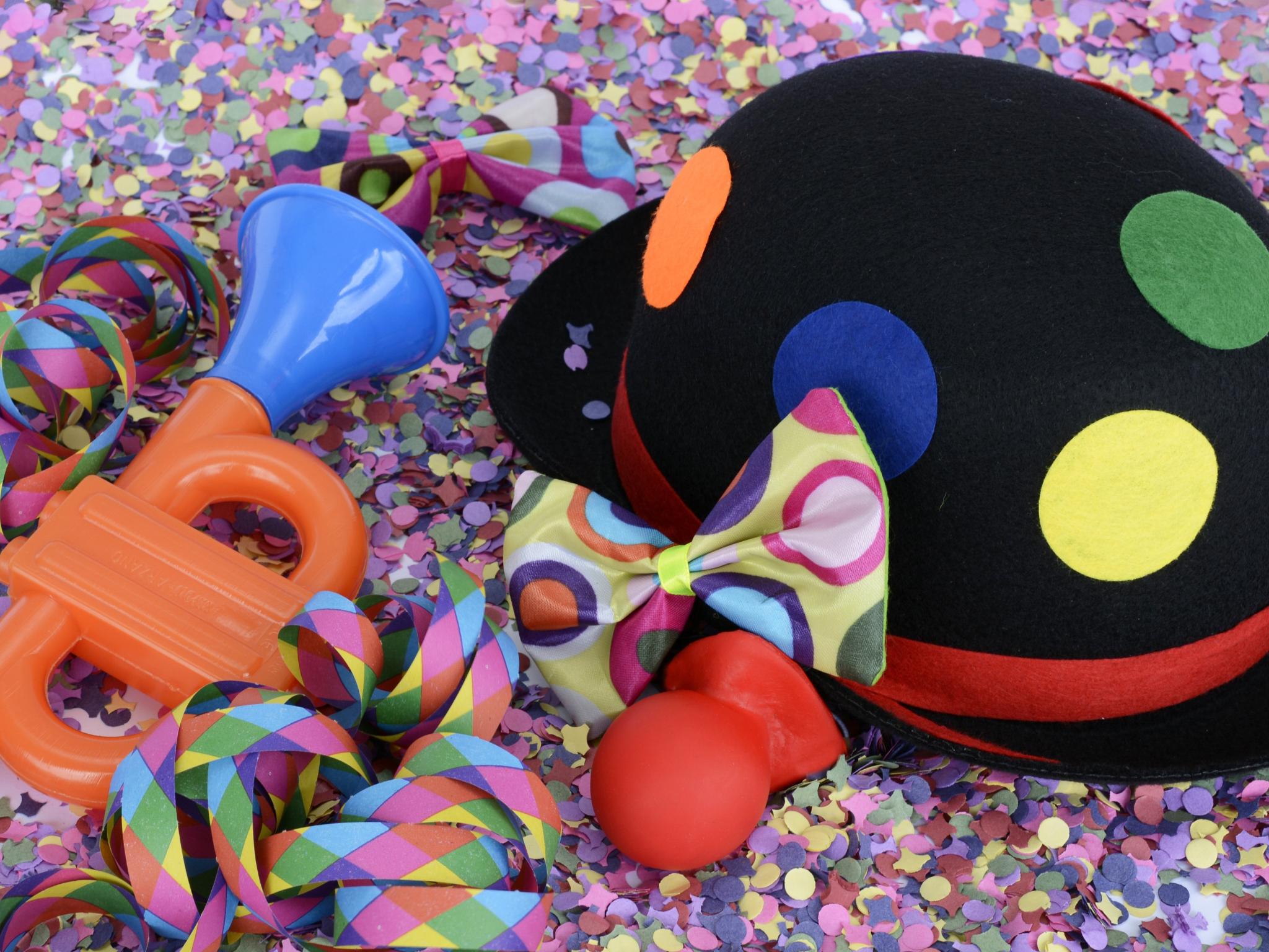 auf dem Bild ist ein schwarzer Clownhut mit bunten Kreisen zu sehen, eine rote Clownnase, eine kleine Tröte und ein paar Luftschlangen