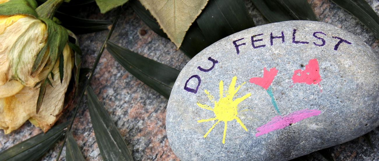 ein mit einer Sonne, Herz und Blume bemalter Stein auf dem Du fehlst geschrieben steht