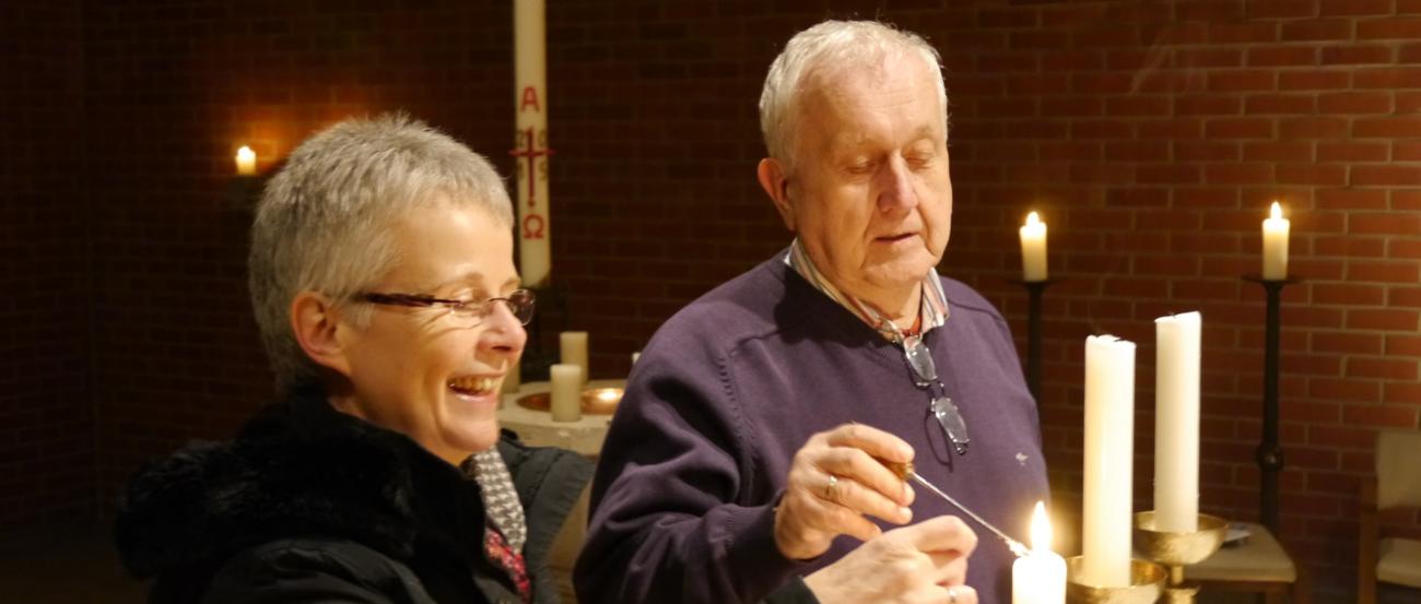 Zwei ältere Menschen zünden gemeinsam Kerzen in einer Kirche an.