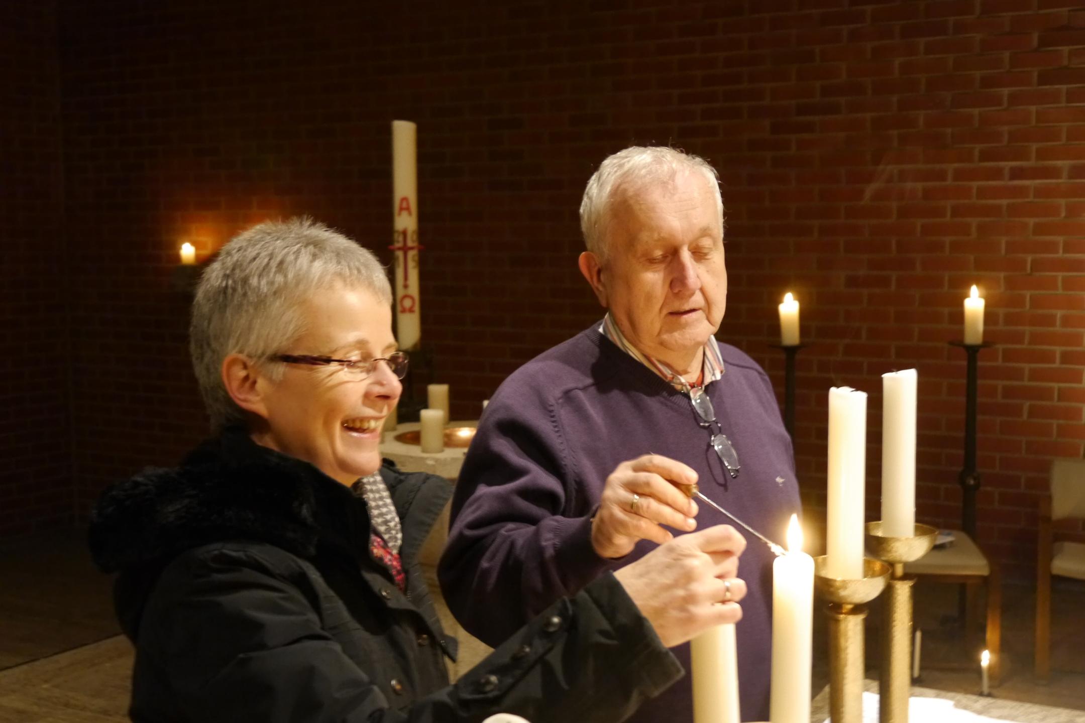 Zwei ältere Menschen zünden gemeinsam Kerzen in einer Kirche an.