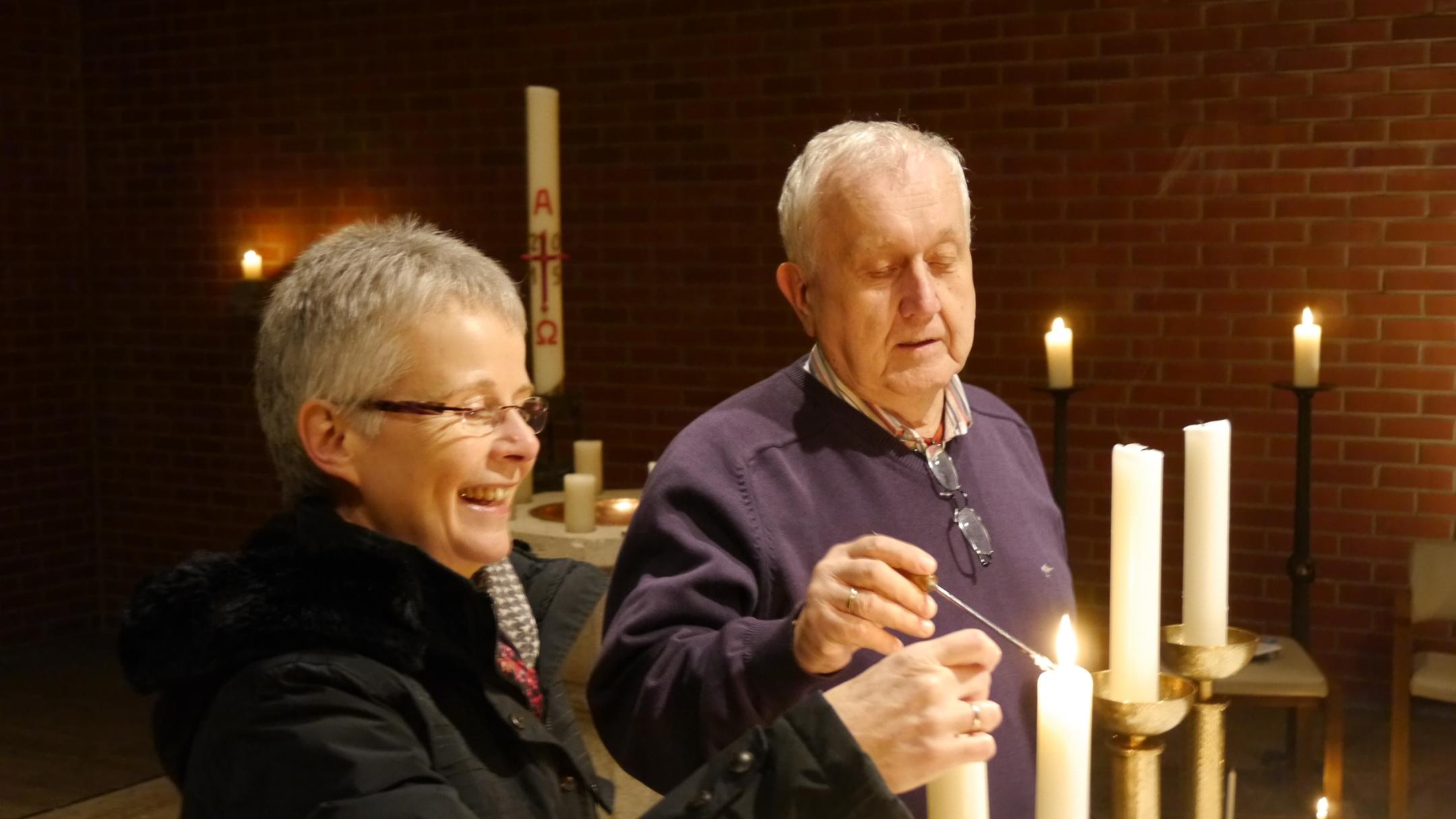 Zwei ältere Menschen zünden gemeinsam Kerzen in einer Kirche an.