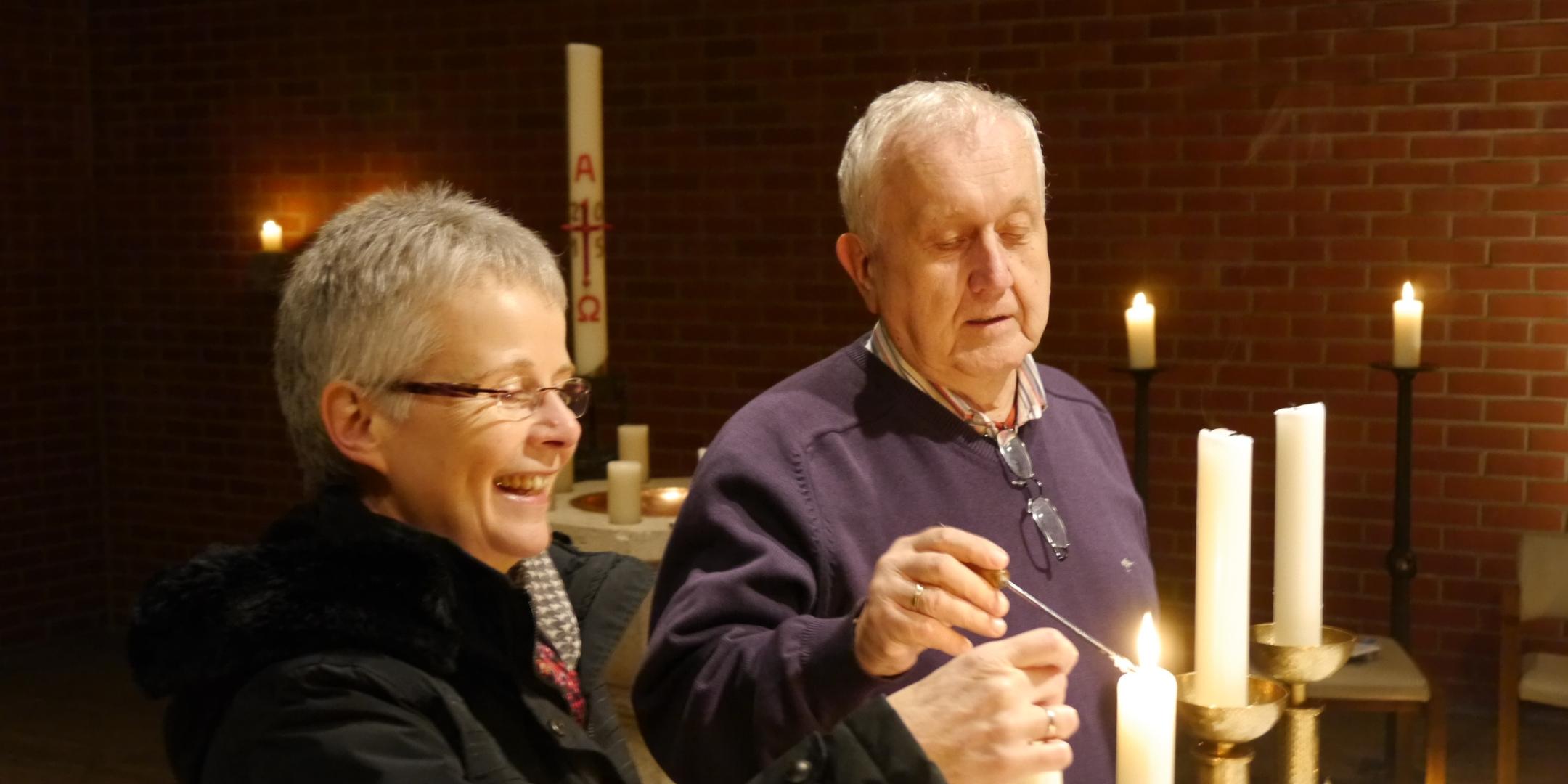 Zwei ältere Menschen zünden gemeinsam Kerzen in einer Kirche an.