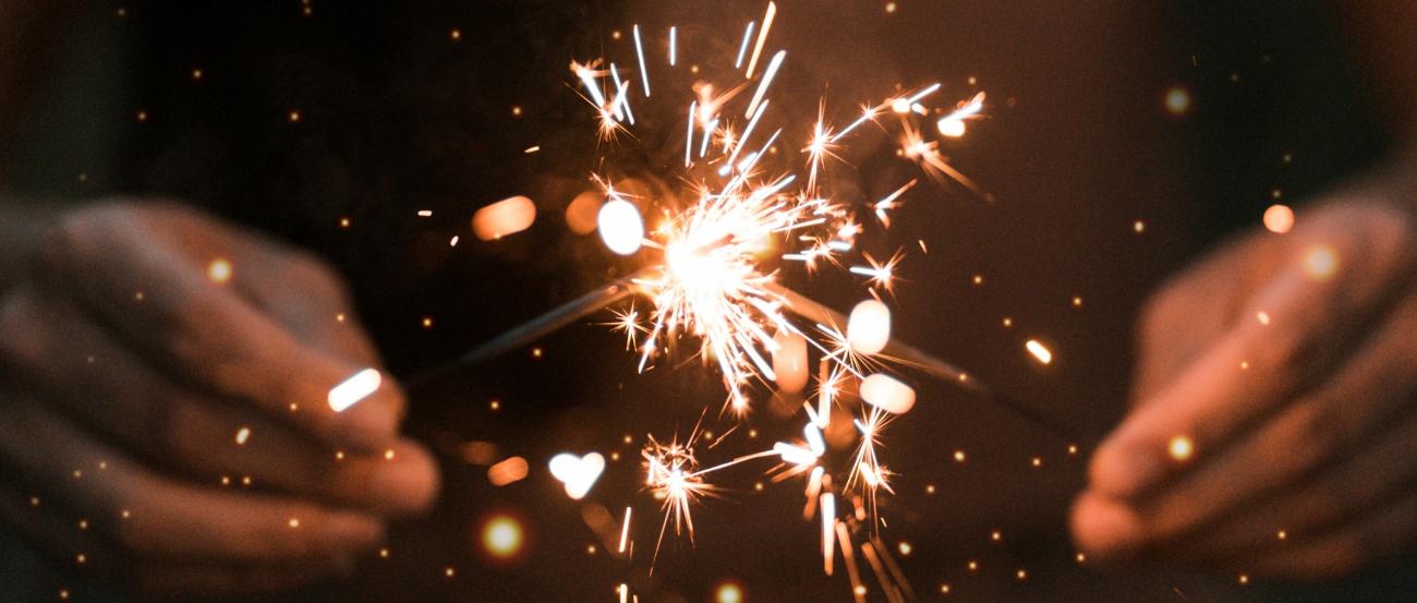 eine Person hält zwei Wunderkerzen in den Händen, die Funken versprühen