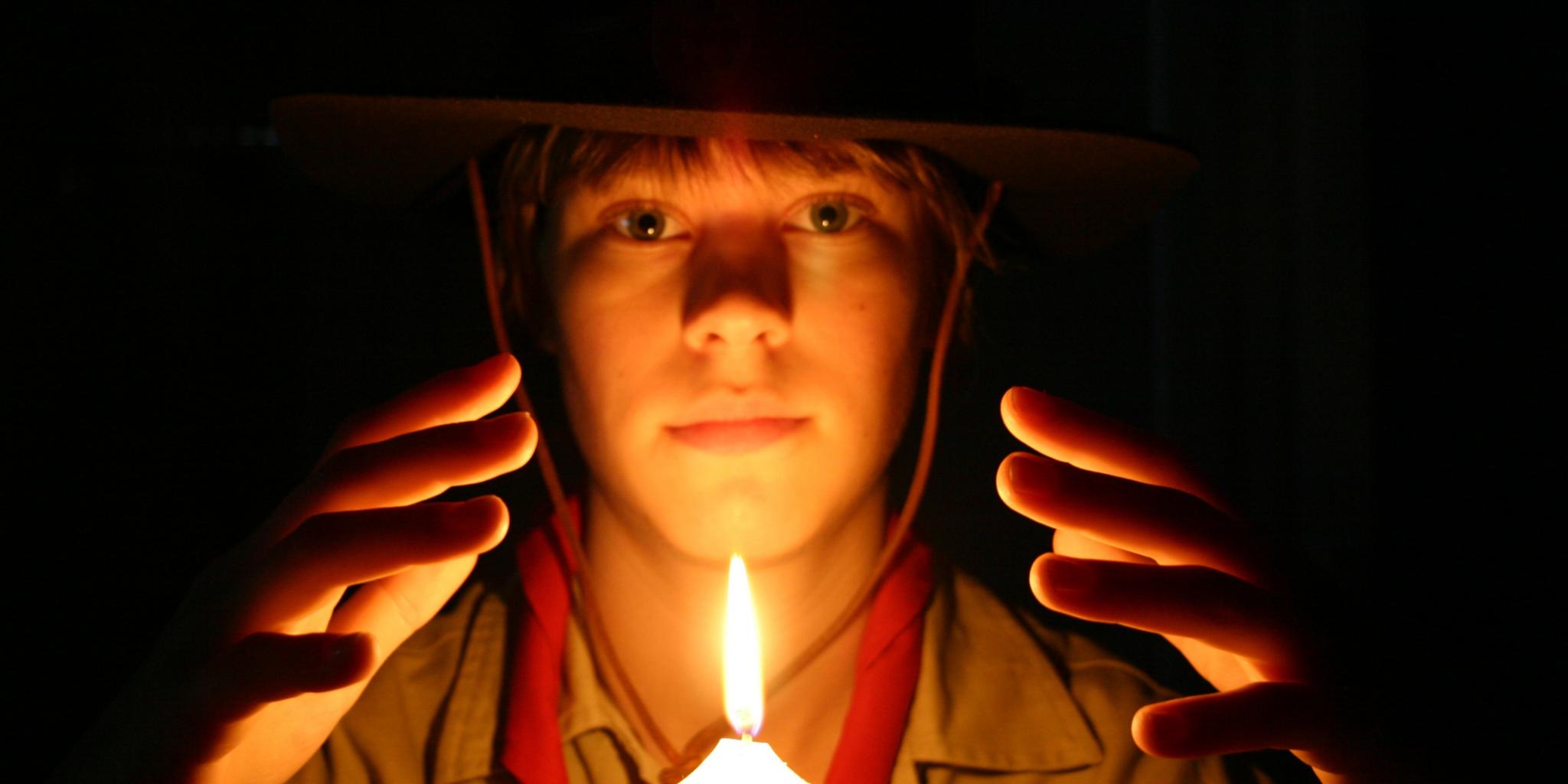 ein Junge in Pfadfinderkleidung hält seine Hände schützend über eine angezündete Kerze
