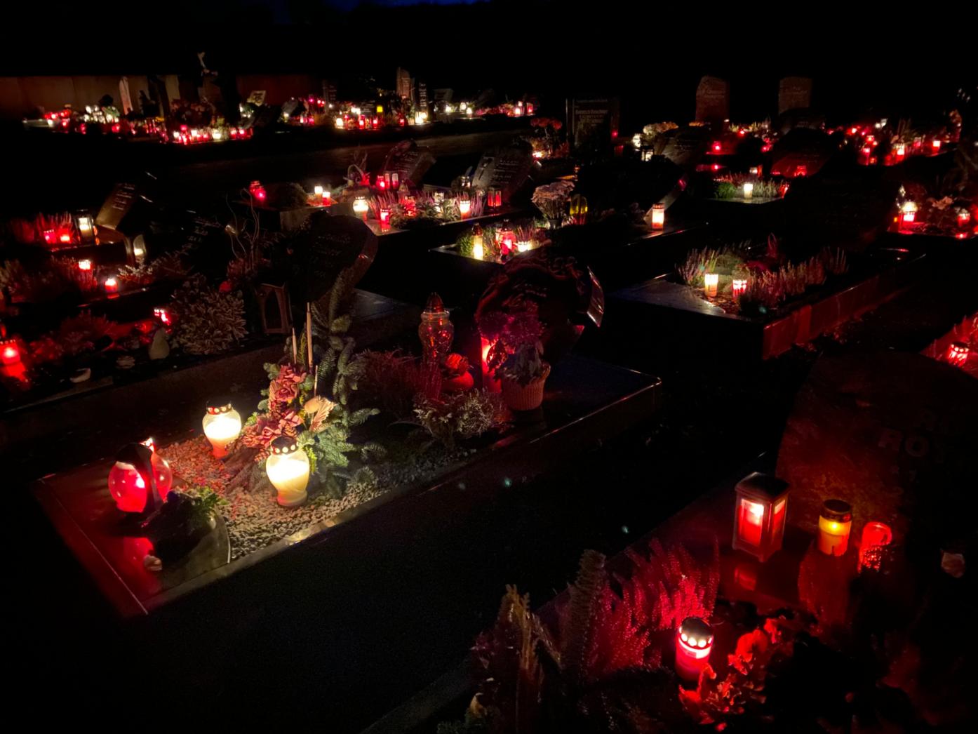 Das Foto zeigt einen Friedhof mit kerzenerleuchteten Gräbern in der Dunkelheit
