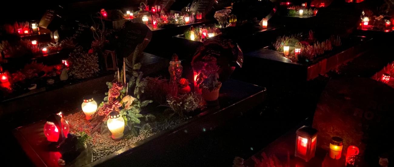 Das Foto zeigt einen Friedhof mit kerzenerleuchteten Gräbern in der Dunkelheit