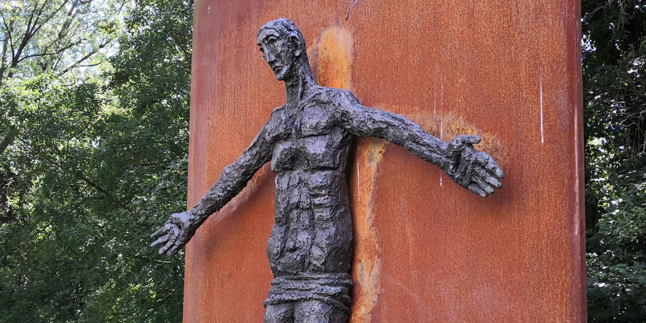 eine aus Bronze gestaltete Figur des Auferstandenen an einer rostfarbenenen Wand