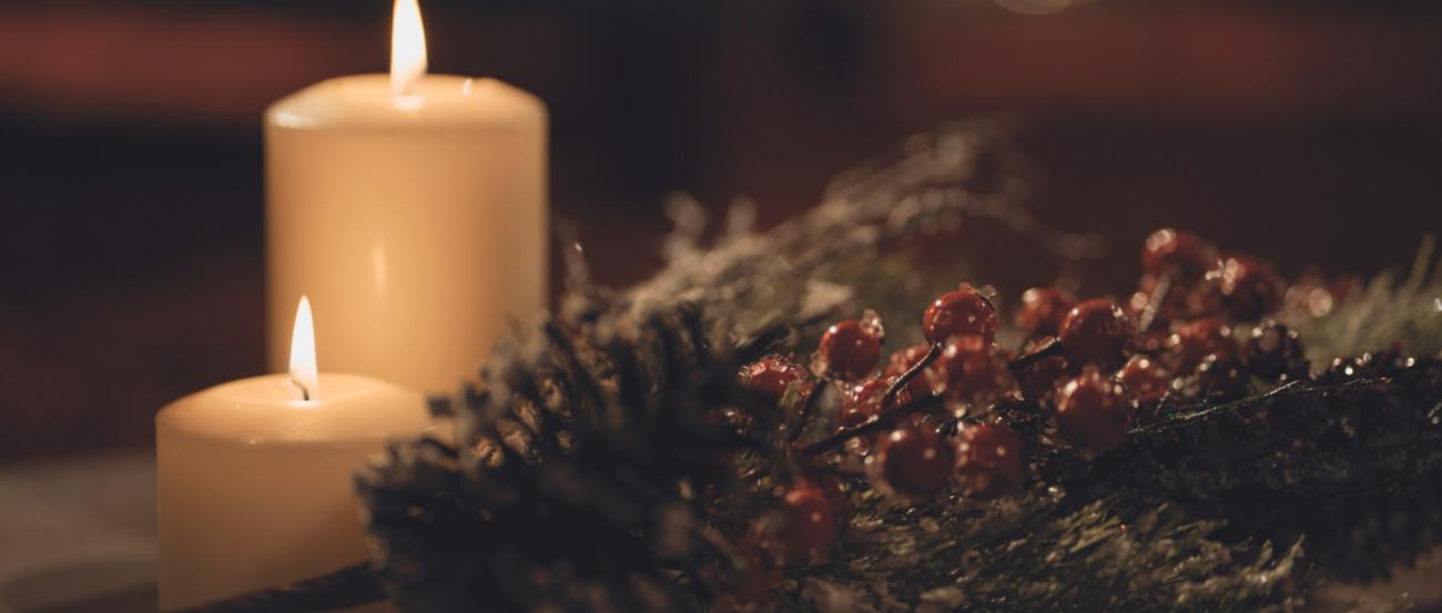 2 angezündete weiße Kerzen, daneben ein Adventszweig mit roten Beeren