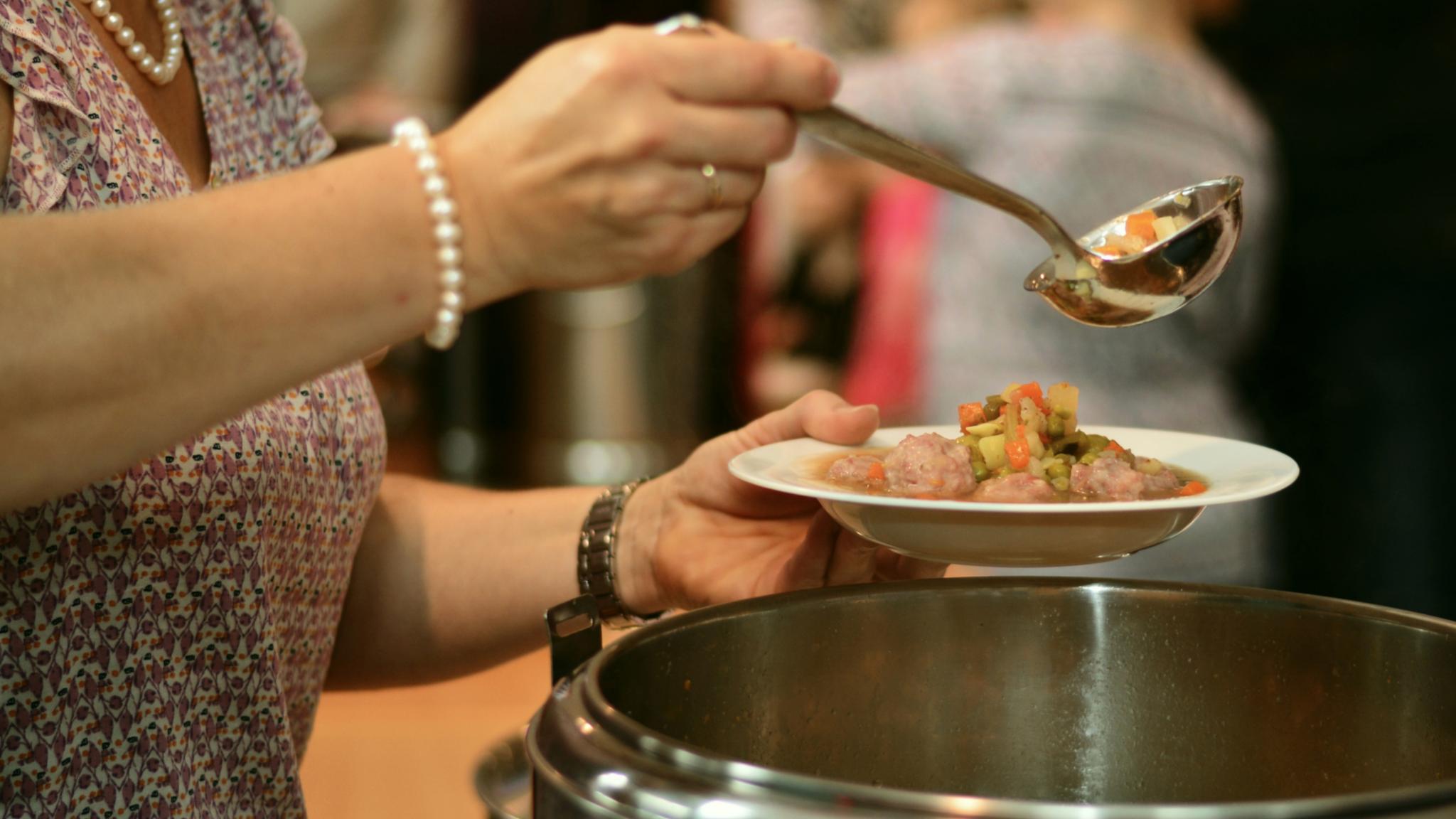 eine Frau füllt aus einem Topf einen Suppenteller mit Suppe