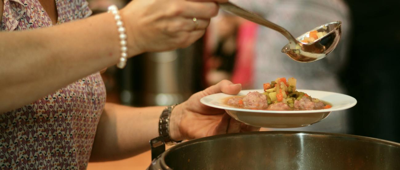 eine Frau füllt aus einem Topf einen Suppenteller mit Suppe