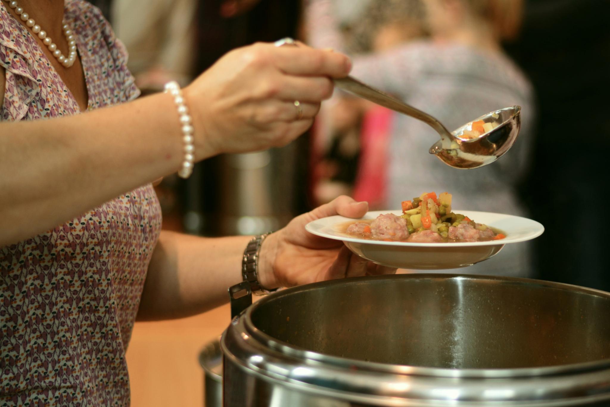 eine Frau füllt aus einem Topf einen Suppenteller mit Suppe