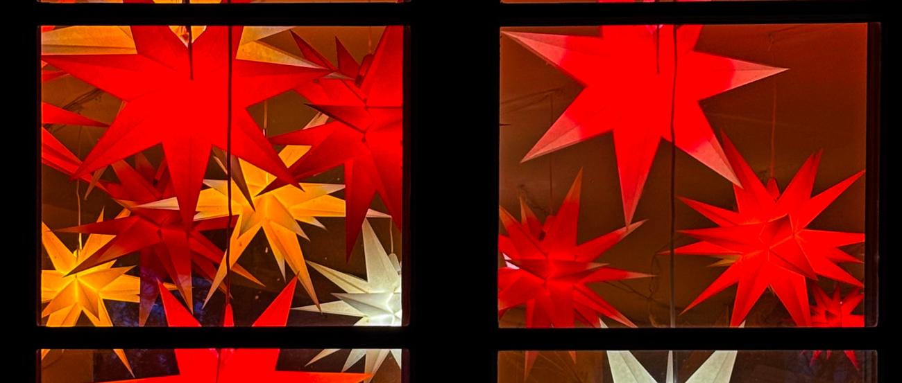 wir schauen auf ein Fenster, dass mit vielen roten, orangen, und 2 weißen Sternen geschmückt ist