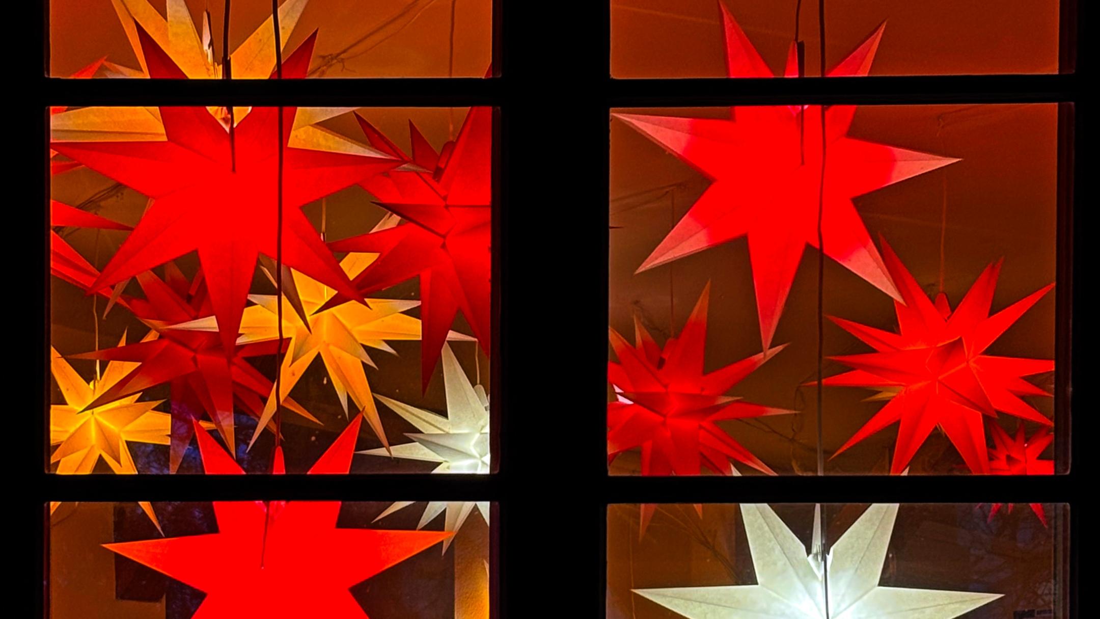 wir schauen auf ein Fenster, dass mit vielen roten, orangen, und 2 weißen Sternen geschmückt ist